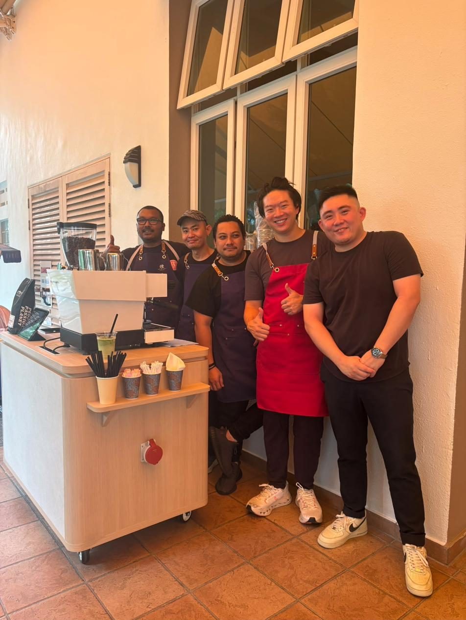 The Kemuri team in aprons beside the wooden coffee cart and espresso machine at an outdoor event