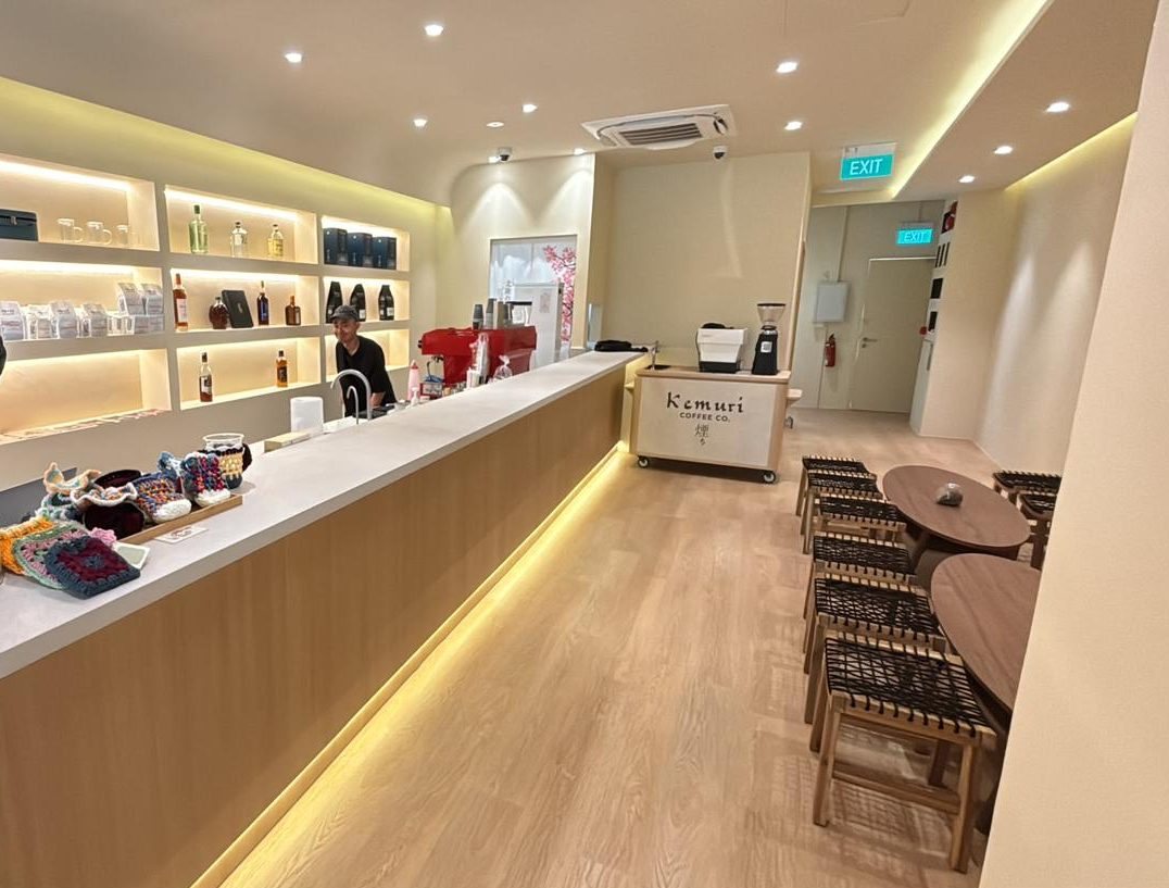 The Kemuri counter with warm under-lighting, backlit shelves of coffee bags, and woven stools along the wall